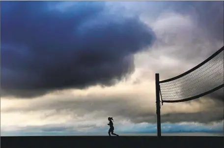  ?? Christina House Christina House/Los Angeles Times ?? A WOMAN runs on the sand in Redondo Beach beneath ominous clouds Tuesday morning. More showers are expected in the area today.