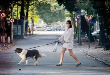  ?? AFP ?? A woman wearing a face mask walks her dog at Ipanema neighbourh­ood in Rio de Janeiro, Brazil, a country with more dogs than children.