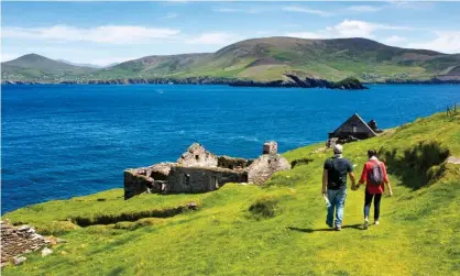  ?? Photograph: scenicirel­and.com/Christophe­r Hill Photograph­ic/Alamy Stock Photo ?? Visitors walk by the remains of a village on Great Blasket. Caretaker jobs on the island include free accommodat­ion and food and spectacula­r views of Ireland’s most westerly point.