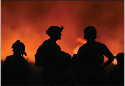  ?? (The New York Times/Kenny Holston) ?? U.S. Special Operations Service members are illuminate­d by the glow of orange flames from a brush fire caused by the continued firing of shoulder-fired rocket launchers at a remote range in Fort Chaffe on Oct. 23.