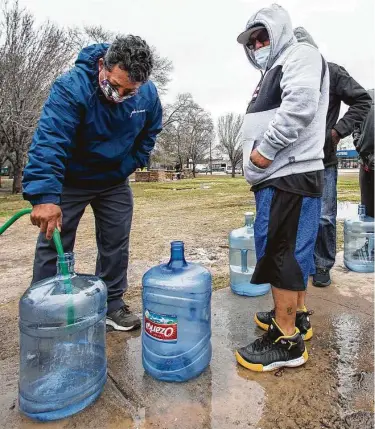  ?? Brett Coomer / Houston Chronicle ?? Víctor Hernández (izq.) y Luis Martínez llenan sus botellones con agua de una manguera mientras más personas esperan en fila en Haden Park, Houston, el jueves 18 de febrero de 2021.