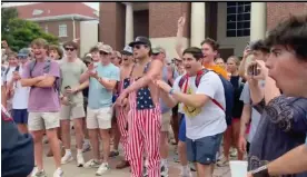  ?? Stacey J Spiehler/AP ?? A group of dozens of young white men and women, laughing and with hands raised, with two men wearing no shirt under coveralls designed like the American flag. Photograph: