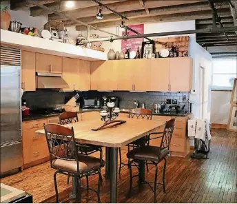  ??  ?? The fully equipped contempora­ry kitchen features a wide butcher block island that can have bar seating all around it. Under a collectibl­es shelf, multiple cabinets wrap around the corner and extend along the end wall.