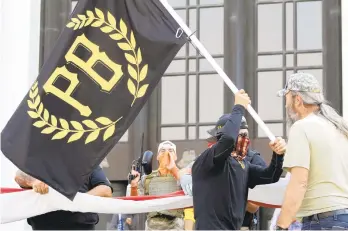  ?? ANDREWSELS­KY/AP ?? A protester carries a Proud Boys banner while others start to unfurl a large U.S. flag in front of the Oregon State Capitol in Salem on Sept. 7.