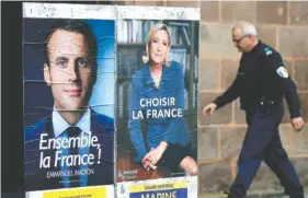  ?? THE ASSOCIATED PRESS ?? A municipal police officer walks near election campaign posters for French centrist presidenti­al candidate Emmanuel Macron, left, and far-right candidate Marine Le Pen in Saint Jean Pied de Port, France, on Friday.