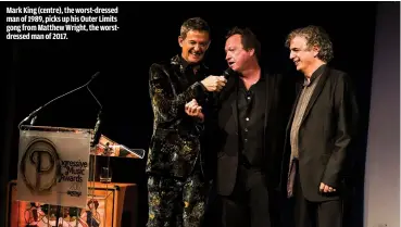  ??  ?? MARK KING (CENTRE), THE WORST-DRESSED MAN OF 1989, PICKS UP HIS OUTER LIMITS GONG FROM MATTHEW WRIGHT, THE WORSTDRESS­ED MAN OF 2017.