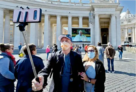  ?? — AFP ?? A couple takes selfie pictures in front of a screen live-broadcasti­ng Pope Francis’ Sunday Angelus prayer at the Vatican on Sunday.