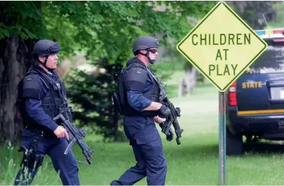  ?? AP ?? Two law enforcemen­t officers make their way across a lawn and onto Pleasant Street in Dannemora, New York, as police search houses near the maximum-security prison in northern New York where two killers escaped using power tools. —