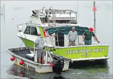  ?? SEAN D. ELLIOT/THE DAY ?? Mike Lamperelli, right, rides along Friday as Spicer’s Marina employees tow his restored 1975 Ray Hunt-designed Chris-Craft 30-foot Sportsman boat to the slip in Noank. Lamperelli has spent 16 years restoring the rare boat.