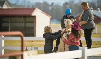  ?? JOHN C. CLARK/FREELANCE PHOTOS ?? Volunteers assist a rider with mounting Suzie Q in the outside riding area at Dream Catchers. One volunteer leads while the others walk on each side to help guide the horse.