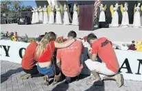  ?? TAIMY ALVAREZ/SUN SENTINEL ?? Kallie Marklo, Mychal Bradley, Zack King and Anthony Ard kneel in prayer in front of 17 angels representi­ng those who died in the shooting at Marjory Stoneman Douglas High School in Parkland.
