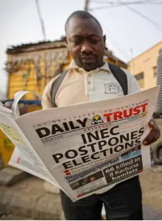  ??  ?? FIRST TO PRINT: A man at a newspaper stand in Kano, northern Nigeria, reads a copy of a newspaper which managed to print the news of the postponeme­nt in time