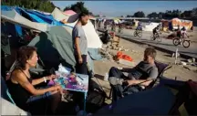  ?? The Associated Press ?? From left, David Pirate, Richard Ramirez and Eric Koehler, who are homeless, pass time outside their tents after emptying a bottle of vodka as a group of cyclists ride along the Santa Ana River trail in Anaheim, Calif.