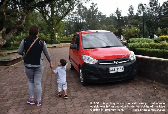  ?? Photo by Redjie Melvic Cawis ?? ILLEGAL. A park goer and her child are puzzled after a vehicle was left unattended inside the vicinity of the Rose Garden in Burnham Park.