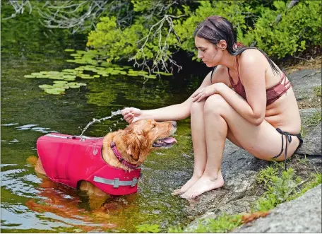 ?? SEAN D. ELLIOT/THE DAY ?? Anita Anderson of Pawcatuck splashes water on friend Jules Vig’s golden retriever, Lola, as she joins Vig, from Redding, and Elizabeth Miskar, from Danbury, cooling off in the waters of Billings Lake in North Stonington on Wednesday.