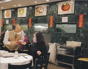  ?? Dania Maxwell Los Angeles Times ?? SERVER Tony Huang, left, receives a red envelope from customer Olivia Chang at Taste of MP in Monterey Park. Lina Situ, the co-owner, said she never considered delaying the tradition.