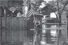  ?? JABIN BOTSFORD/WASHINGTON POST ?? A man carries a flag to place on his truck Monday as members of a team with the United States Coast Guard perform search and rescue through flood waters in Lumberton, N.C., in the aftermath of Hurricane Florence. As the region’s waters rise, environmen­tal hazards are materializ­ing in the Carolinas.