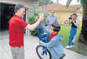  ?? SUSAN STOCKER/SOUTH FLORIDA SUN SENTINEL ?? Neil Goldberg, a Broadway director and children’s book author, gives Noman Mujtaba, 10, a recent arrival from Afghanista­n, a high-five as he presents him with a new bike Wednesday in Davie.