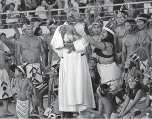  ??  ?? A priest holds a baby as clergy and indigenous people wait Friday for the arrival of Pope Francis in Puerto Maldonado, Madre de Dios province, Peru. Francis met with several thousand indigenous people gathering in a coliseum in Puerto Maldonado, the...