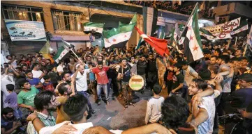  ??  ?? Syrians dance, chant slogans and strike drums while others and wave flags of Turkey and the opposition, as they protest against the Syrian government during a demonstrat­ion in Binnish in the rebel-held northern Idlib province.