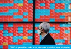  ?? —AFP ?? TOKYO: A pedestrian looks at an electronic quotation board displaying companies’ stock prices on the Tokyo Stock Exchange in Tokyo.