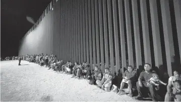  ?? GREGORY BULL AP ?? Migrants wait along a border wall in August after crossing from Mexico near Yuma, Arizona. A surge in migration from Central and South American countries in September brought the number of illegal crossings to the highest level ever recorded in a fiscal year, according to a recent report by U.S. Customs and Border Protection.