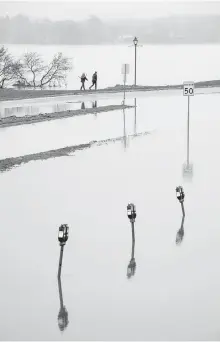  ??  ?? Pedestrian­s navigate a narrow parcel of land as floodwater­s from the St. John River swamp downtown Fredericto­n on Monday.