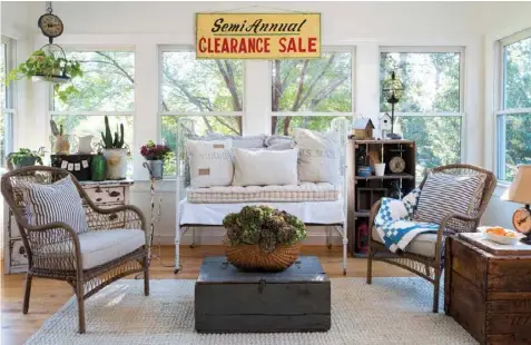  ??  ?? An old crib becomes a daybed in the sunroom and adds to the relaxed seating options. A trunk used as a coffee table introduces a dark, grounding hue, while the bright Clearance Sale sign brings a burst of energy to the neutral palette. An old scale hung in the corner makes for an eye-catching plant holder. Amy also repurposes pails and buckets to host potted plants and employs ironstone pitchers to hold small garden tools.