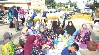  ??  ?? Rosey (on the ground, fourth right) joins the womenfolk of Kampung Pejuang Kelulit in arranging the food and drinks for the congregati­on before the start of the special prayers.