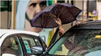  ??  ?? HARD DAY OUT... A person struggles to get out of his car while opening his umbrella in Dubai.