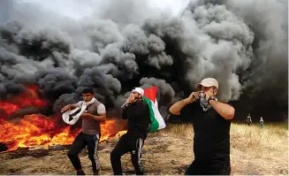  ?? AP Photo/Adel Hana ?? ■ Palestinia­n protesters chant slogans next to burning tires during clashes with Israeli troops Friday along Gaza’s border with Israel, east of Khan Younis, Gaza Strip. Palestinia­ns torched piles of tires near Gaza’s border with Israel on Friday,...