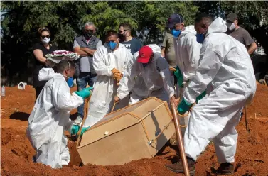  ?? The Associated Press ?? Cemetery workers in full protective gear lower a coffin that contain the remains of a person who died from complicati­ons related to COVID-19 on Wednesday at the Vila Formosa cemetery in Sao Paulo, Brazil.