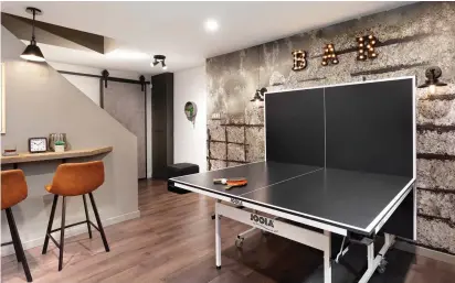  ??  ?? L'impression­nant mur à l'aspect bétonné qui rehausse la zone du pingpong ajoute du caractère au décor, tandis que l'enseigne lumineuse crée une ambiance des plus festives. Pour pallier la présence de matériaux sombres, la designer a choisi de multiplier les sources d'éclairage.