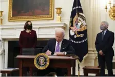  ?? AP ?? STRAIGHT TO WORK: President Biden signs executive orders Thursday about the coronaviru­s while joined by Vice President Kamala Harris and Dr. Anthony Fauci.