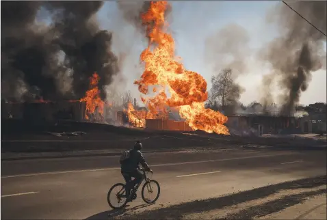  ?? A man rides his bike March 25 past flames and smoke rising from a fire following a Russian attack in Kharkiv, Ukraine. (AP/Felipe Dana) ??