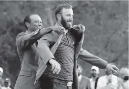  ?? CHARLIE RIEDEL AP ?? Tiger Woods helps Masters champion Dustin Johnson with his green jacket after his record-setting victory at the Masters golf tournament, which was held in November.