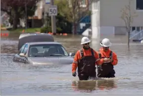  ?? The Canadian Press ?? Workers wearing hip waders pass a submerged car as they walk on Rue Saint-Louis in Gatineau, after flooding caused by significan­t rainfall.