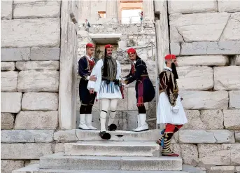  ??  ?? The Evzones are helped to descend the Acropolis archeologi­cal site in Athens after the Greek flag ceremony. An emblematic image of the country for a century and a half, this elite corps turns 150 this year. — AFP