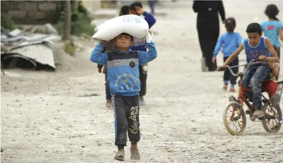  ?? Reuters ?? A boy carries food aid given by the World Food Programme in Syria, where prices increased by more than 200 per cent last year