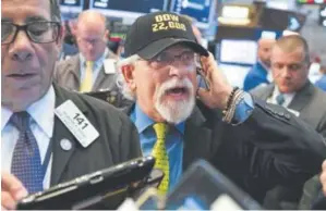  ?? Richard Drew, The Associated Press ?? Trader Peter Tuchman, center, works on the floor of the New York Stock Exchange on Wednesday. A big gain for Apple sent the Dow Jones industrial average above 22,000 for the first time.