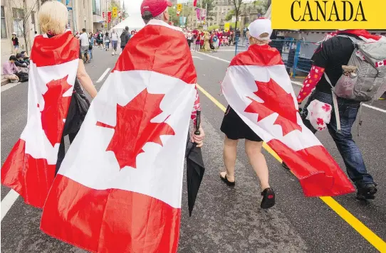  ?? DARREN BROWN / POSTMEDIA ?? Revellers wrap themselves in the flag as they walk along Wellington Street in downtown Ottawa during celebratio­ns of a somewhat wet Canada Day in the capital July 1.