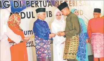  ??  ?? Taib, flanked by Rohani on his right and Fatimah, gives away the contributi­on to a boy, as (from right) Abang Shamsuddin and Sharifah Hasidah look on.