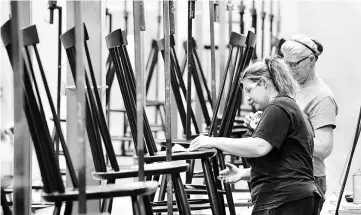  ??  ?? Tritapoe, left, and Virginia Remsburg prepare chairs for finishing in the factory at Gat Creek. The US$18 million operation builds high-end, wood furniture and employs 140 people. — WP-Bloomberg photos