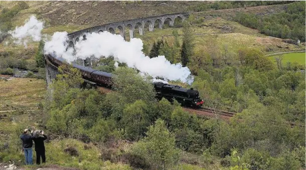  ??  ?? RISK: Two onlookers take photograph­s of The Jacobite steam train as it crosses the Glenfinnan Viaduct from a safe distance, but other have not been so sensible