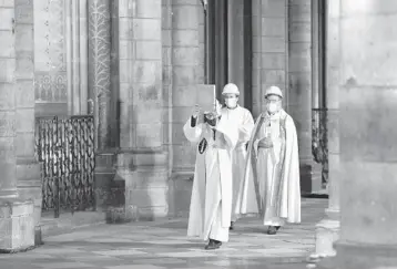  ?? CHRISTOPHE ENA/AP ?? Notre Dame rector Patrick Chauvet leads a helmeted procession during a Holy Thursday service at Notre Dame Cathedral in Paris. The ceremony, held days before Easter, involved a foot-washing ritual symbolizin­g Jesus’ willingnes­s to serve. The 858-year-old church is still being rebuilt following a dramatic April 2019 fire in which the sprire crumpled.