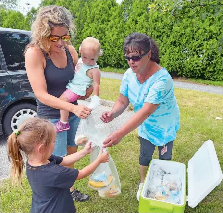  ?? TIM MARTIN/THE DAY ?? Debora Maurice, right, a prep cook with the Groton Public Schools Food Service, passes out a free lunch to Lora Flowers of Groton and her children Edie, 19 months, and Lena, 4, on Friday at the Poquonnock River Walkway in Groton. The meals are provided...