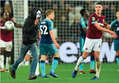  ??  ?? West Ham’s Declan Rice throws the ball at a masked pitch invader during last night’s League Cup defeat to Tottenham