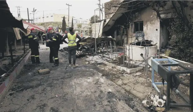  ??  ?? 0 A volunteer and firemen stand outside the burnt-out school for refugee children, part of the One Happy Family project, on Lesbos yesterday