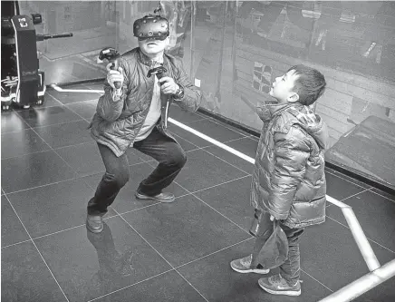  ??  ?? A boy watches his dad as he wears virtual-reality glasses while playing a game at the Leke VR Park in Beijing, China.