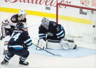  ?? TREVOR HAGAN
THE CANADIAN PRESS ?? Edmonton Oilers’ Connor McDavid (97) scores on Jets goaltender Connor Hellebuyck with Josh Morrissey trailing during NHL action in Winnipeg on Tuesday. The Oilers won, 5-4 in overtime.
